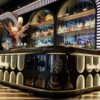 art deco illuminated curved bar counter with oval backlit panels and arched wine shelving for cocktail lounge speakeasy