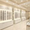 Minimalist All-White Built-In Eyewear Display Wall Unit | LED Recessed Optical Frame Display Racks With Central Brand Logo Panel & Base Storage Cabinets For Premium Optical Store Interior