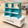 Mobile teal white trapezoidal multi-tier retail display cart with storage cabinet and caster wheels Lexio Display for cosmetic perfume boutique mall pop-up