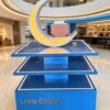 Blue three-tier LED edge lighted retail island display stand with illuminated crescent decor Lexio Display for shopping mall pop-up and product promotion