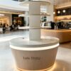 Four-tier round retail display stand wood grain tapered base with warm LED lighting white shelves Lexio Display for café bakery and mall food retail