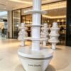 Minimalist all white four-tier cylindrical column retail display stand tapered base Lexio Display for retail store and mall pop-up product promotion