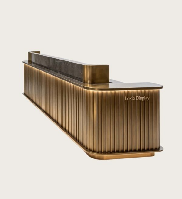 Fluted antique brass L-shaped reception desk with dark marble top and LED ambient light, luxury office lobby front counter Lexio Display for high-end corporate interior