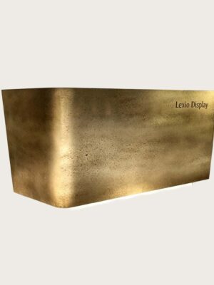 Chamfered angular reception desk with textured forged aged brass metal cladding, floating base LED glow luxury office lobby front desk Lexio Display for premium commercial fit‑out