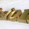 Mirror gold 3D metal brand logo letters floating on white reception wall