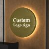 Round brushed gold metal backlit logo sign with halo LED light mounted above office reception counter