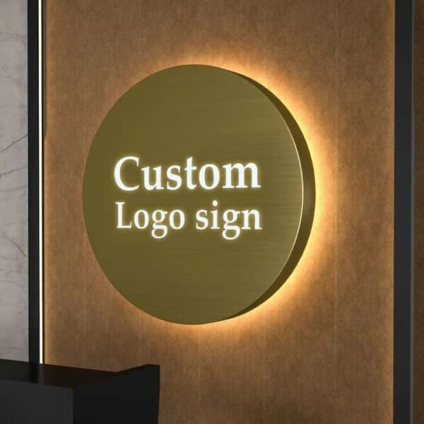 Round brushed gold metal backlit logo sign with halo LED light mounted above office reception counter