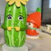 Customized fiberglass display (1) Isolated render of cute green cucumber fiberglass mascot statue, cartoon crying expression, yellow flower and hands on white base
