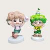 Factory workshop photo of two cartoon nature kids fiberglass mascot sculptures, pink outfit kid holding volleyball, green hair kid with bird and sapling on head, standing on white round bases