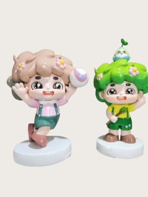Factory workshop photo of two cartoon nature kids fiberglass mascot sculptures, pink outfit kid holding volleyball, green hair kid with bird and sapling on head, standing on white round bases