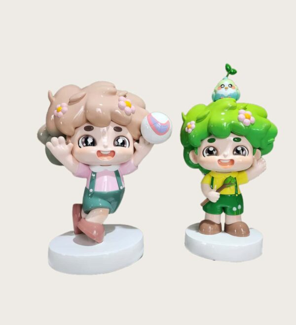 Customized fiberglass display (19) Factory workshop photo of two cartoon nature kids fiberglass mascot sculptures, pink outfit kid holding volleyball, green hair kid with bird and sapling on head, standing on white round bases